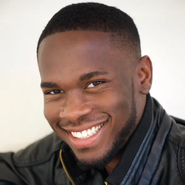 Smiling man wearing a black leather jacket, looking confidently at the camera. The background is light, highlighting the warm and friendly expression.