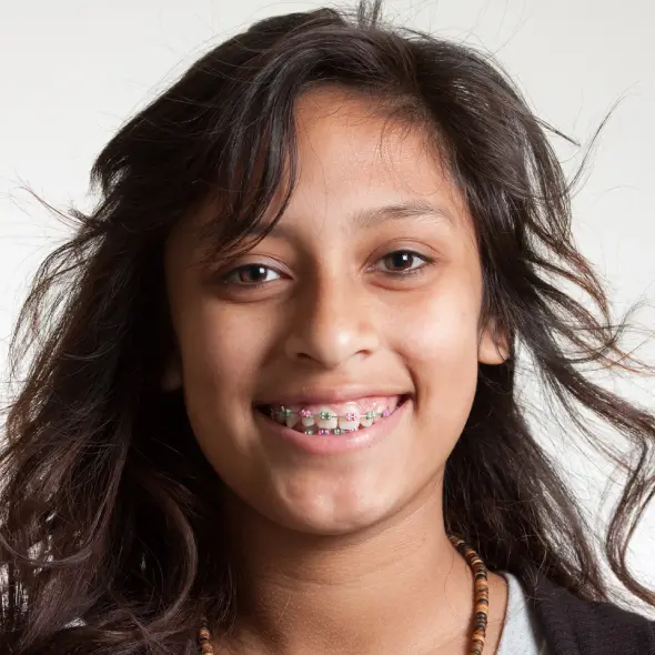 Smiling young person with long, flowing hair and colorful braces. The expression is joyful, conveying a sense of positivity and carefree energy.