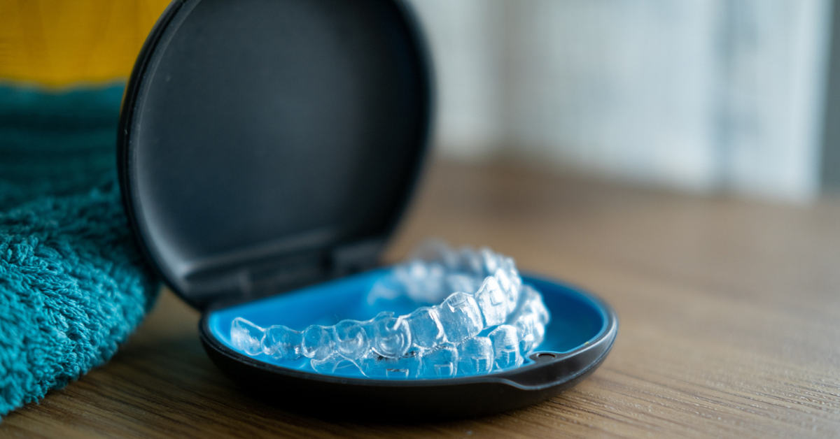 Clear dental Invisalign aligners in an open black and blue case, placed on a wooden surface next to a blue towel, conveying a clean, organized setting.